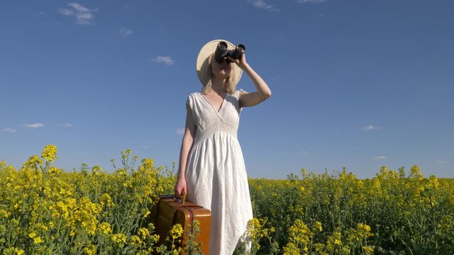 woman in dress with suitcase and binoculars in rapeseed field