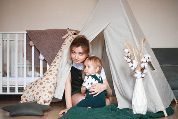 Mother and little son playing children room with play tent.