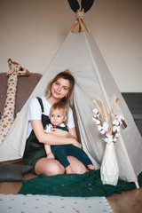 Beautiful mother and baby boy sitting on the floor playing inside the teepee