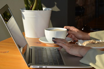 Laptop, women's hands and a Cup of coffee on the table in the cafe.