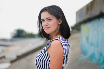 portrait of a young brunette girl in a striped, blue with white, summer dress climbing the stairs and turned over her shoulder. girl walks around the city on a hot summer day