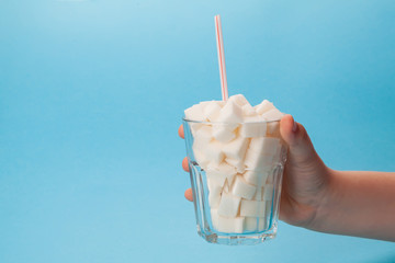 Children's hand holds a glass glass with a tube full of sugar cubes