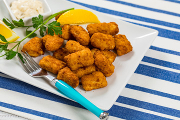 Crispy Fish Bites Snack Size. Deep Fried Pollock Fish Fingers with Tartar Dipping Sauce on a Wooden Board. Selective focus.