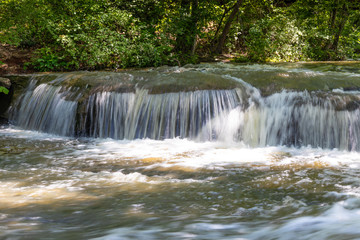 Water cascading over rocks in a woodland stream, sunlight and shade with heavy foliage, horizontal aspect