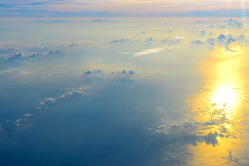 Sun rise in the morning of blue sky above the white clouds and land background with golden light looking through an airplane window