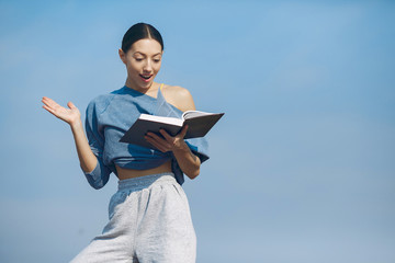 Beautiful girl standing on a sky background. Woman in a blue sweater. Lady with book in her hands
