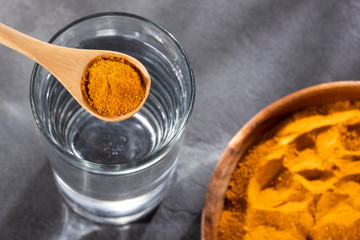 Spoon with organic turmeric and glass of filtered water - Curcuma longa