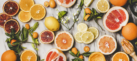Ingredients for cooking Citrus cake. Flat-lay of fresh oranges, lemons, kumquats, grapefruits and blossom flowers over marble background, top view, wide composition. Vegan, clean eating food concept