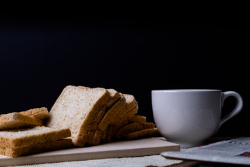 Homemade slide bread with hot coffee cup and newspaper on the wooden with copy space on black background