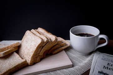 Homemade slide bread with black coffee cup and newspaper on the wooden with copy space on black background.