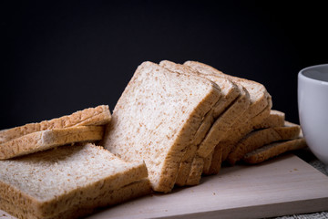 Close-up Homemade slide bread with hot coffee cup and newspaper on the wooden with copy space on black background.
