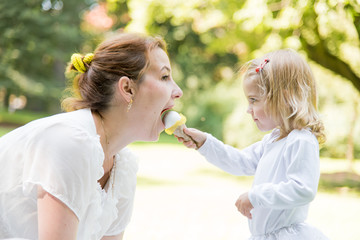 Fototapeta premium Beautiful little girl in a park on a picnic with her mother. Spring sunny concept. Happy mothers day. Happy loving family. Mother and daughter.