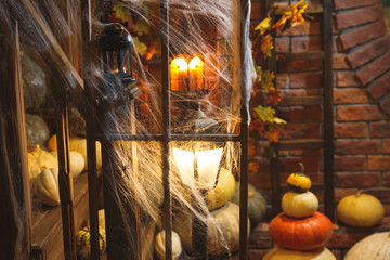 Festive mystical halloween interior. A lot of different pumpkins. Spider web, candles, spiders. Selective focus on the lantern.