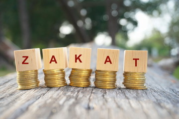 Close up of stacking gold coins and wooden blocks written ZAKAT on nature background and natural lighting. Zakat or Islamic tax concept