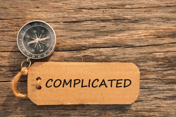 Magnetic compass and paper tag with words COMPLICATED at outdoor. Conceptual image with selective...