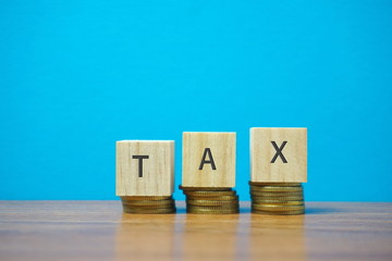 Tax concept : Close up of stacking coins and wooden blocks written TAX with nature lighting