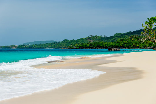 Beach landscape with sand, white foam waves, palm trees, blue sky, turquoise water and clouds, paradise Caribbean coast of Dominican republic 