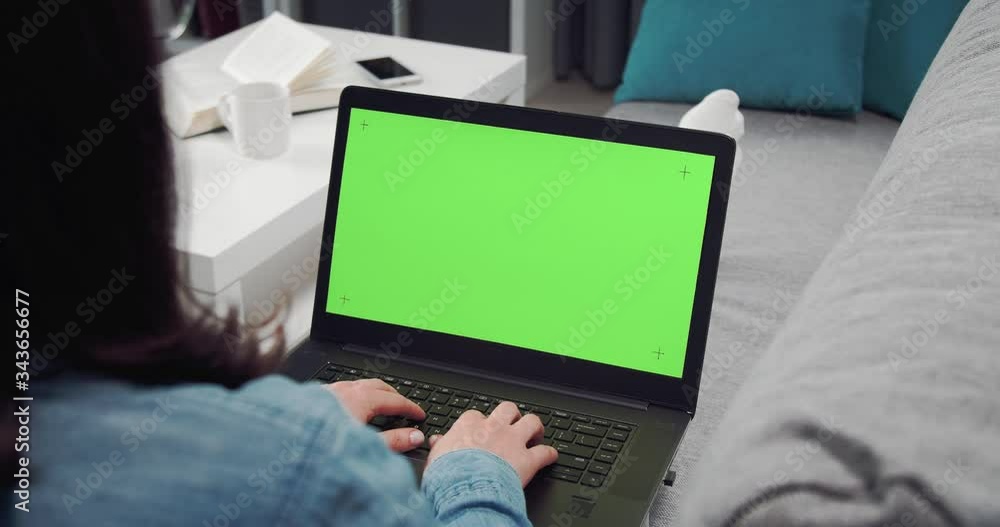 Poster view from back of young girl lying on couch and working on laptop with chroma key screen. space for 
