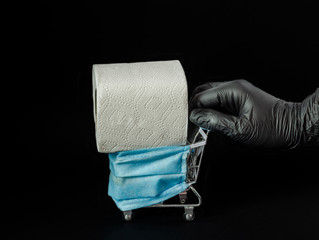 Female hand in a rubber glove rolls a decorative trolley in a protective medical mask, toilet paper on a black background.
