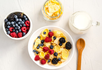 Healthy breakfast with cornflakes, raspberries, blackberries, blueberries, milk and coffee on a white background.