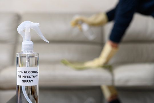 Bottle Of 75 Percent Alcohol Disinfectant Spray With A Man Disinfecting And Cleaning A Sofa At Background