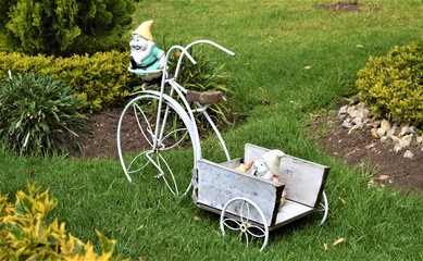 Una pequeña y bonita carreta en forma de cicla, con dos figuras de enanos fabricadas en yeso, adornan el jardín de un conjunto residencial.