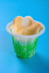 side view cup of orange and green color ice cream with some bites on blue background