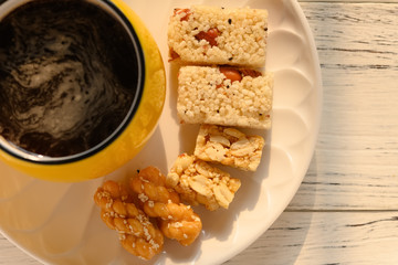 sweet rice puffs blocks and fried dough twists and peanut brittles and cup of coffee on a dish
