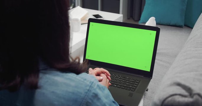 Woman with brown hair in casual outfit having video chat on laptop with chroma key screen. Young lady using digital device for online conversation at home.