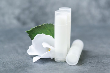 lip balm with flowers in a transparent tube with white contents. DIY lipstick made from natural eco-friendly ingredients. hand made on a gray background - obrazy, fototapety, plakaty
