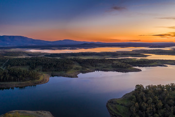 Aerial view of Gabriel y Galan lake at Extremadura countryside. An amazing view during sunset time on a cloudy day. The colors of the sky reflected over the lake waters give an idyllic landscape view
