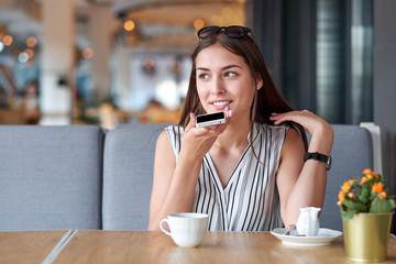 Young business woman talking audio message in phone in coffee shop