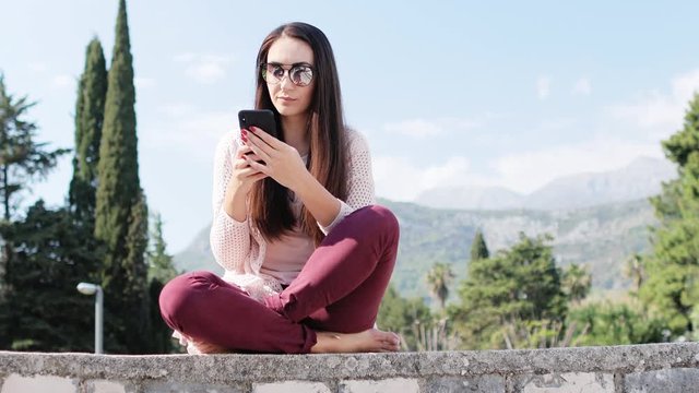 woman using phone outdoors sitting in park with mountains view. Long hair bunette woman texting and using phone outdoors. 