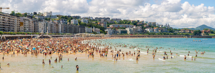 Obraz premium Panoramiczny widok na tłumy latem na plaży San Sebastian w Hiszpanii