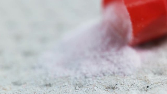 The red capsule lies open on a gray background. A fine white powder spilled out of the tablet. Medical device extreme close-up, real time, camera movement from right to left