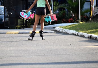 Panor&aacute;mica de las piernas de una chica que carga sus juguetes, mientras recorre una v&iacute;a en sus patines, en una tarde de verano.
