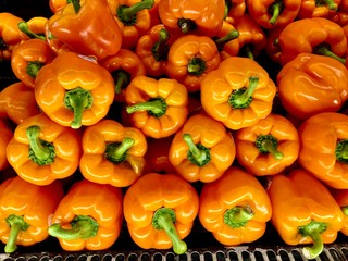 Orange bell peppers with bright green stems in a neat pile.