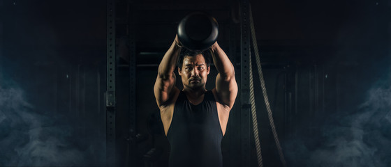 asian athletic strong man having workout and bodybuilding with kettlebell weightlifting backsquat style in gym and fitness center in dark tone