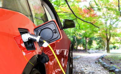 EV Car or Electric car at charging station with the power cable supply plugged in on blurred nature with soft light background. Eco-friendly alternative energy concept