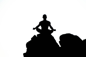 Silhoutte of a man sitting on top of a huge rock in a meditation position. Black and white. The photo looks like an ilustration.