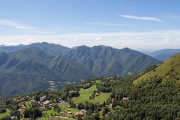 Mountain landscape with village, green slopes, mountains and blue sky on background.