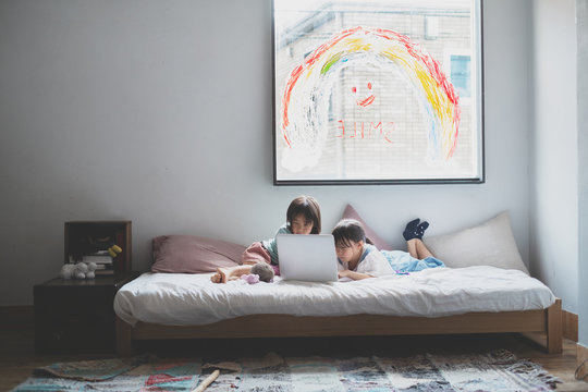 SIMLEの虹が描かれた窓の前、ベッドルームで寝転んでパソコンを見る子供たち