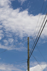 Fototapeta premium Power pole supporting electrical power lines running in three directions, isolated against a blue sky with clouds, vertical aspect