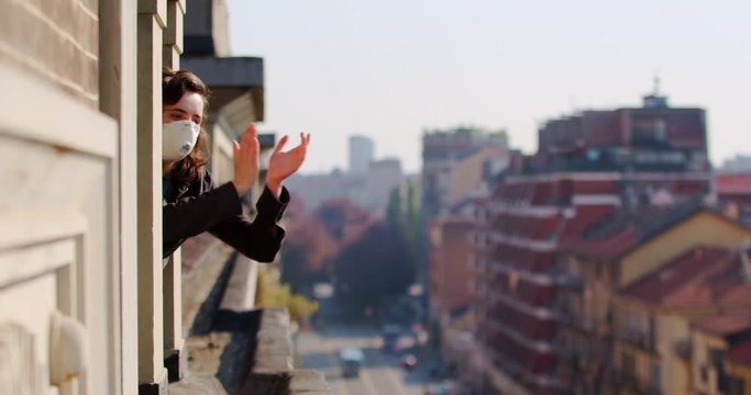 Girl applauds doctors during the coronavirus pandemic in Europe. People look out the window. Quarantine all over the world, a woman sits at home
