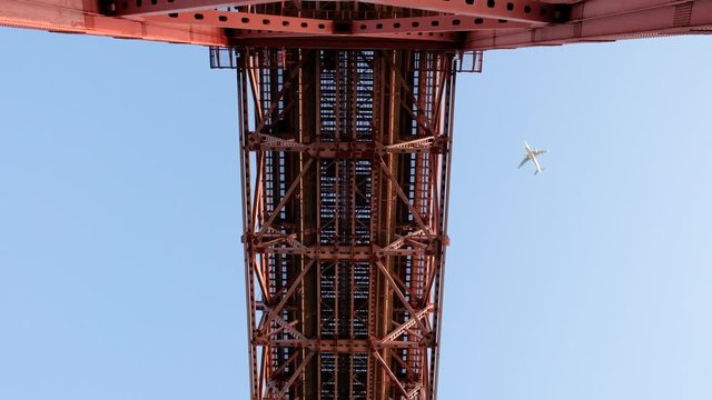 Red bridge from bellow and airplane flying over. Below double deck 25 de Abril Bridge with traffic in Lisbon while the airplane is descending to Lisbon Portela Airport. 