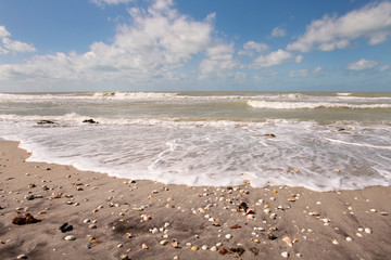 Waves rolling in to shell covered beach with beautiful cloud filled sky