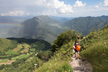 Obraz premium Tourists walking on a trail with rainbow and mountains on background.