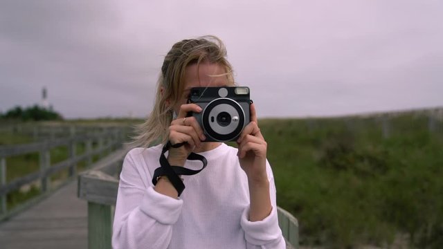 Young hipster girl wanderlust posing while photographing you on contemporary instant camera. Female tourist taking pictures during spare time on nature, youth millennial lifestyle. Slow motion effect
