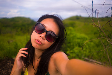 young attractive and cool Asian Korean woman in sunglasses taking selfie with mobile phone enjoying beautiful field landscape view during Summer holidays