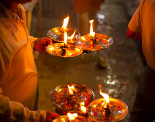 A man holds several lightened oil diya lamps with flower petals in it for performing puja on Diwali or Ganga Aarti